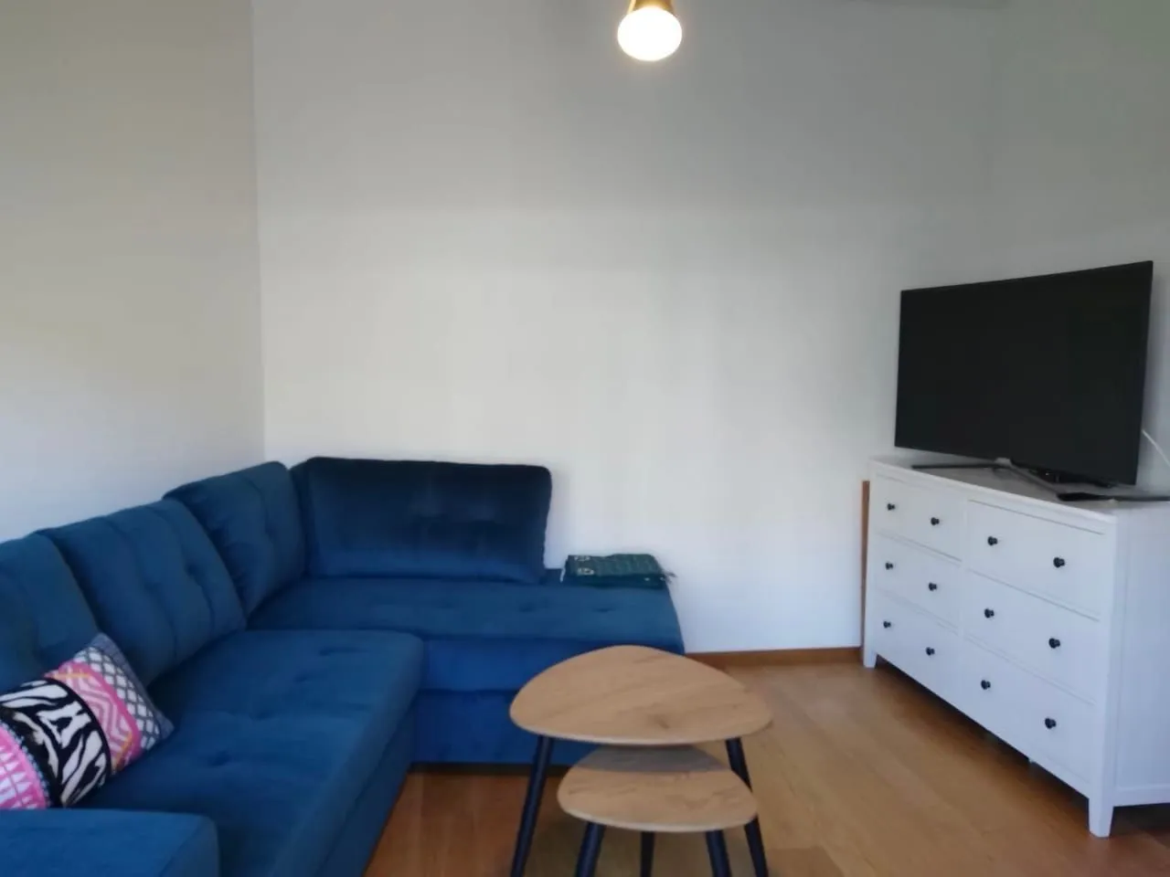 Dnevna soba sa plavom ugaonom garniturom, belom komodom i televizorom.