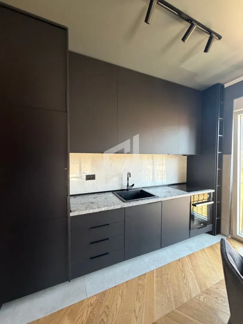 Modern dark kitchen with built-in appliances and a sink.