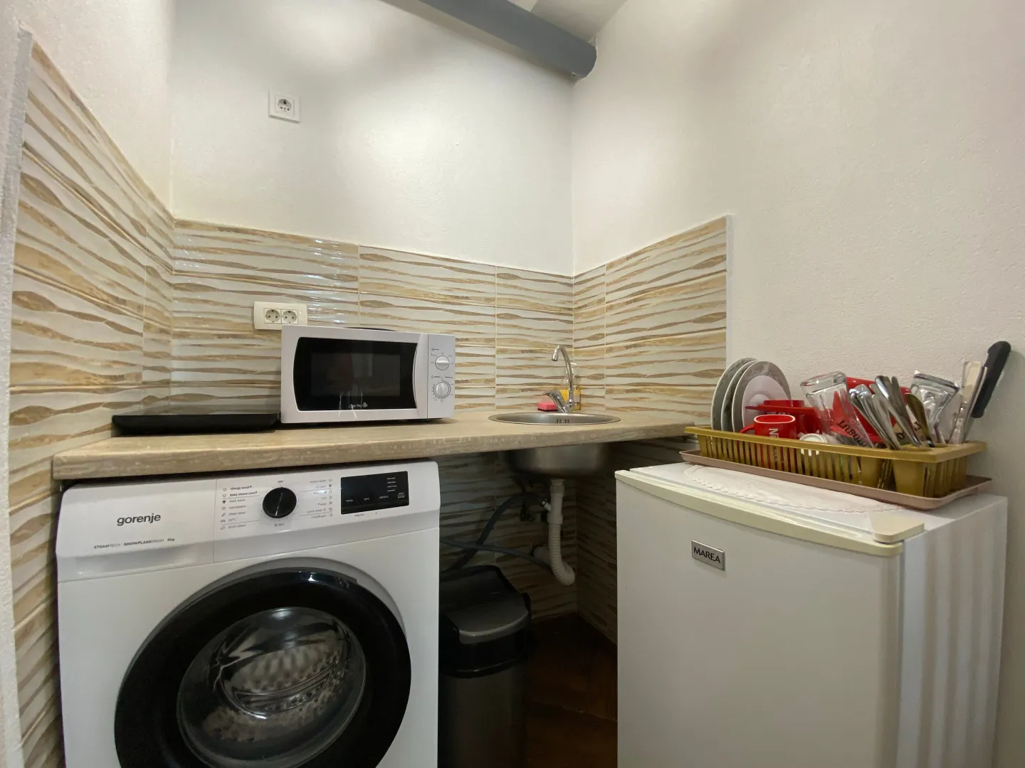 Small kitchen equipped with a sink, washing machine, microwave, and small refrigerator.