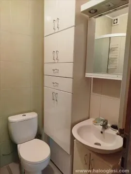 Manje kupatilo sa umivaonikom, WC šoljom i visokim belim ormarićem. - image 5