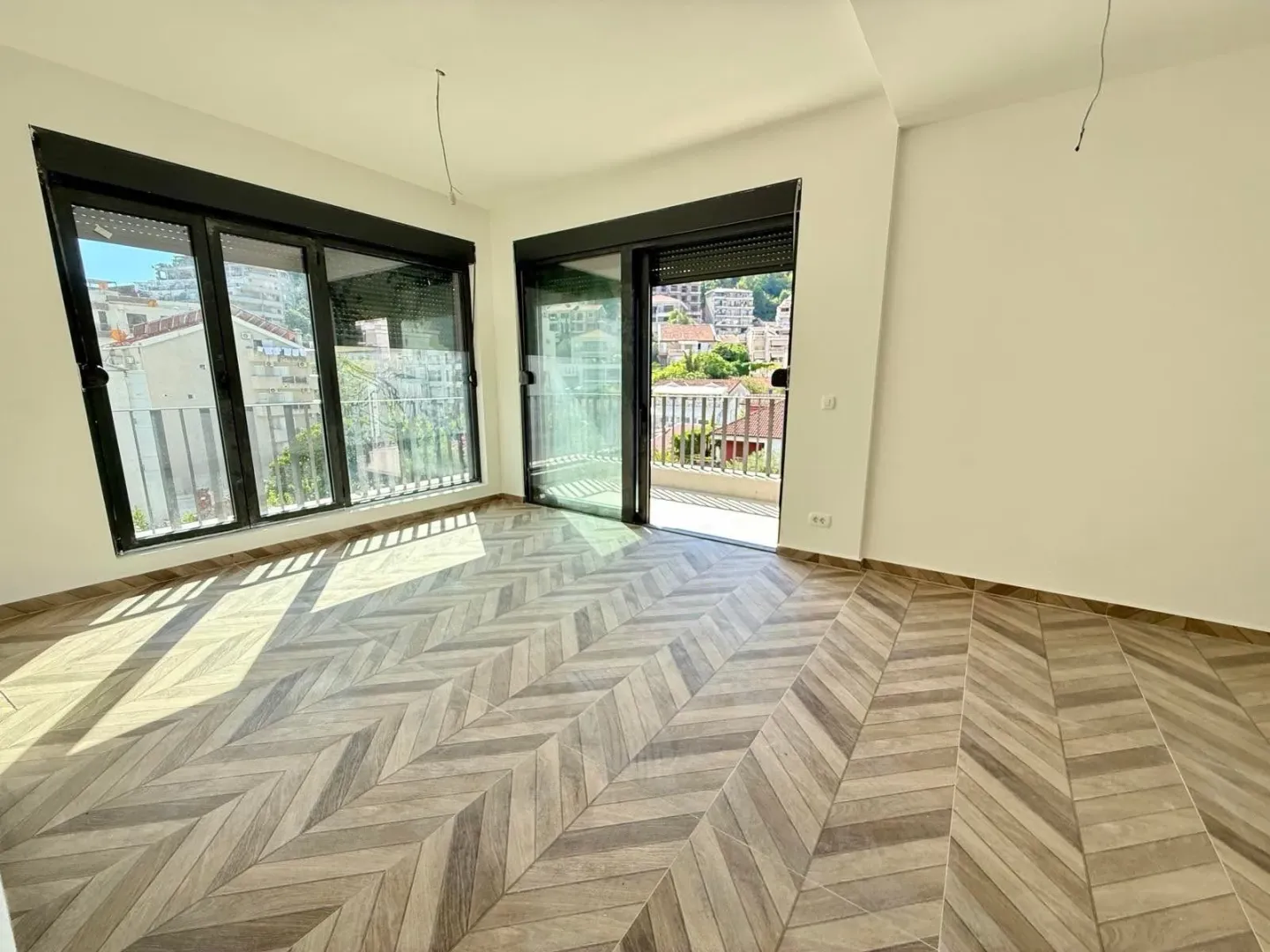 Empty room with parquet flooring and large windows leading to the terrace.