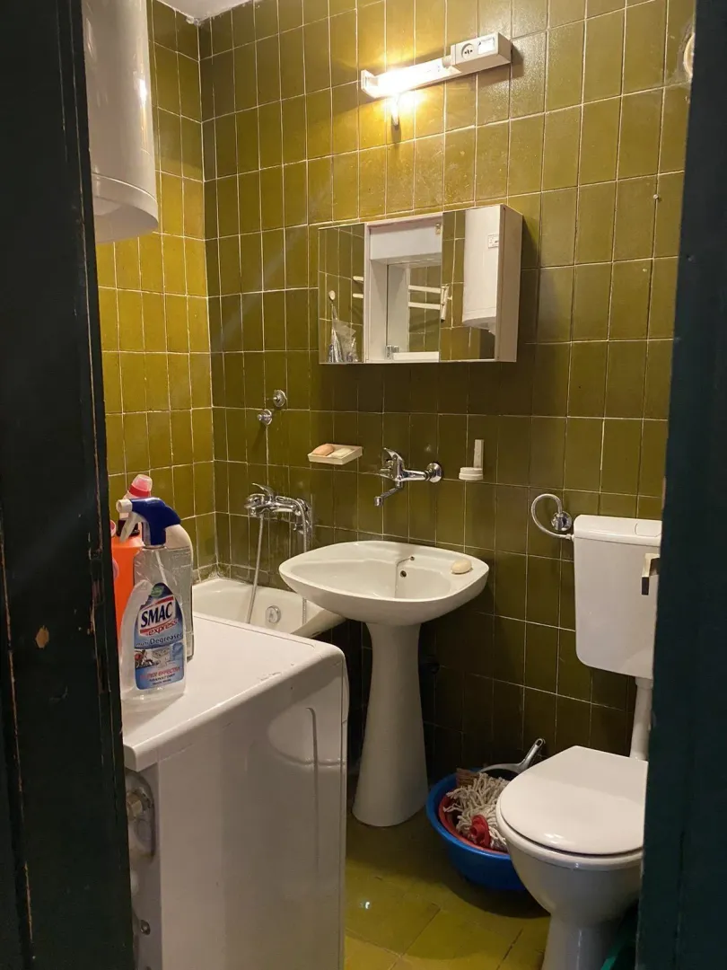Jednostavno kupatilo sa zelenim pločicama, lavaboom i toaletom.