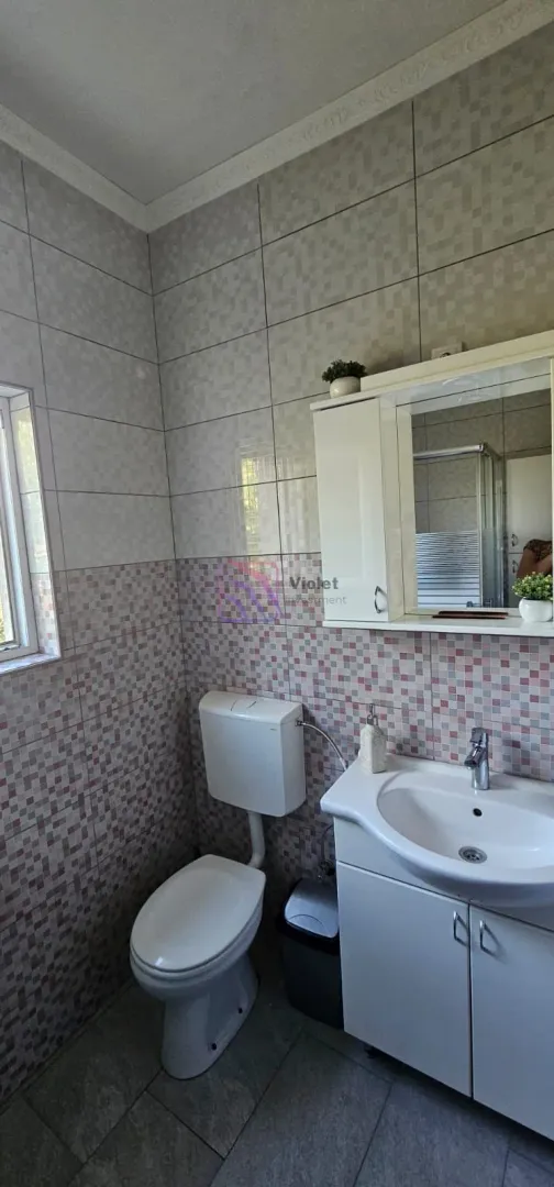 Kupatilo opremljeno umivaonikom, WC šoljom i zidnim ormarićem sa ogledalom.