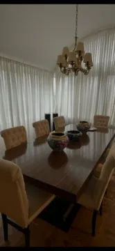 Trpezarija sa velikim drvenim stolom i tapaciranim stolicama pored prozora sa belim zavesama. - image 14