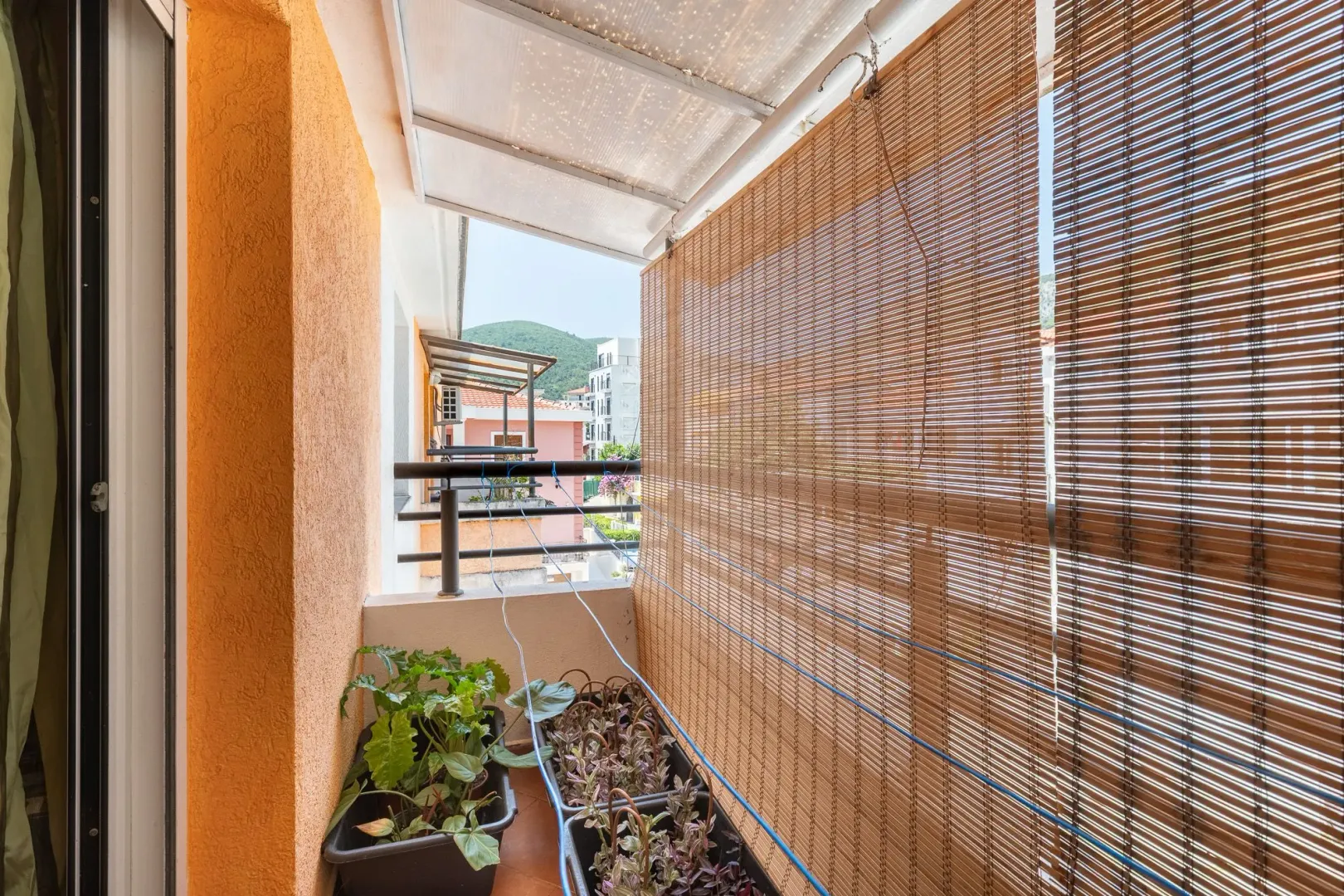 Natkriveni balkon sa saksijama sa biljkama i rolo zavjesom za zaštitu od sunca.