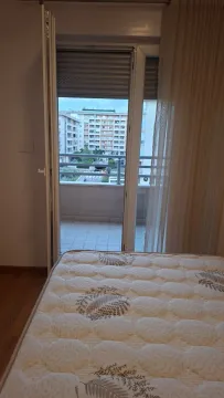 Pogled iz spavaće sobe sa krevetom prema balkonu i zgradama u okruženju. - image 5