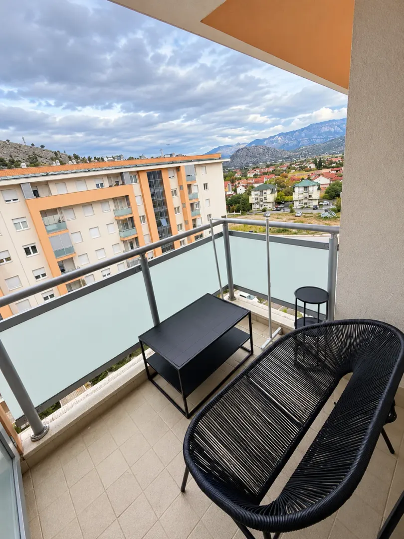 Namješten balkon sa garniturom za sjedenje i pogledom na okolne zgrade i planine.