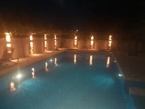 Illuminated swimming pool in the backyard at night. - image 9