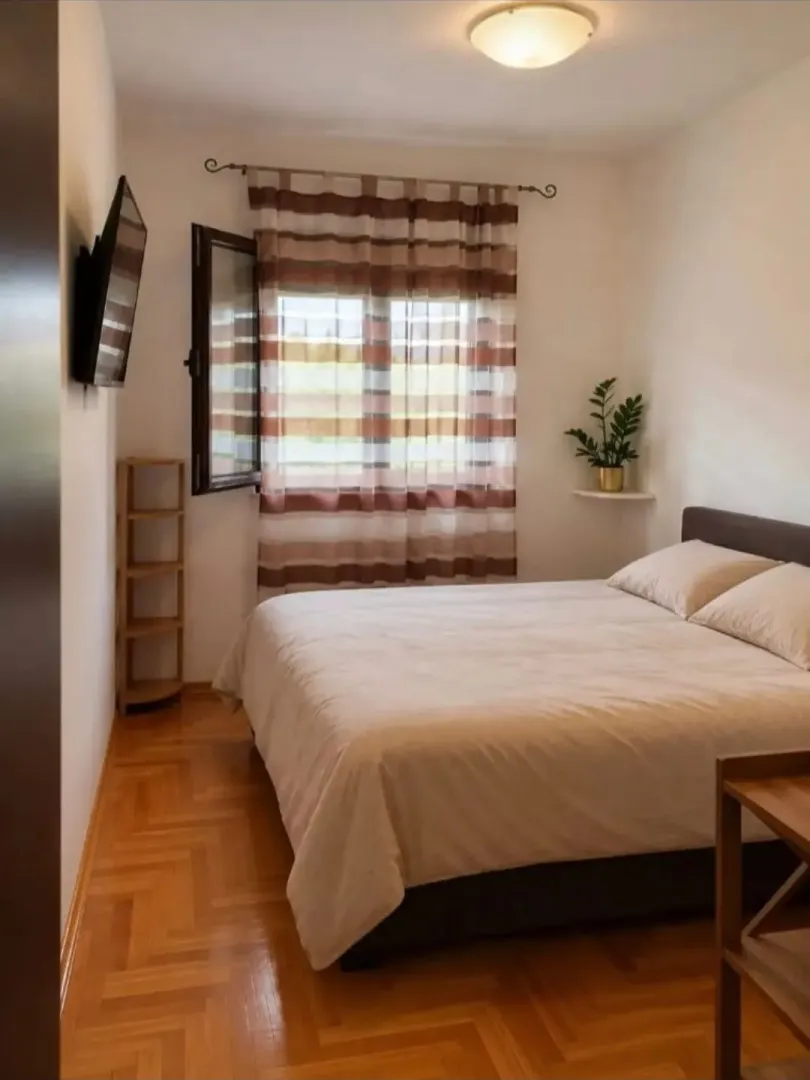 Uređena spavaća soba sa bračnim krevetom, drvenim podom i prozorom.