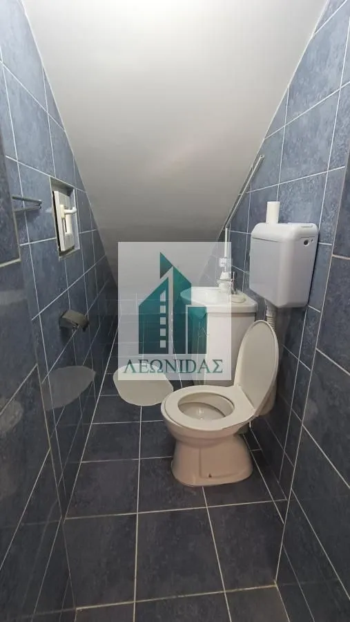 Manje kupatilo obloženo pločicama sa toaletom i umivaonikom pod kosim krovom.