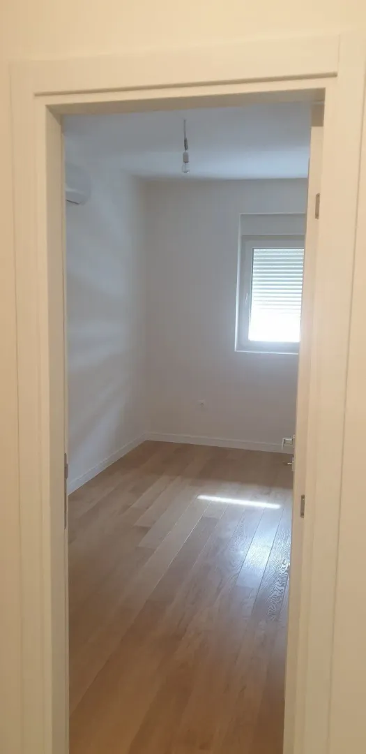 A view through a doorway into an empty room with light wooden flooring.