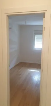 A view through a doorway into an empty room with light wooden flooring. - image 2