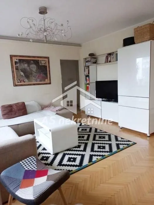 Living room with a sofa, TV, and white furniture units.