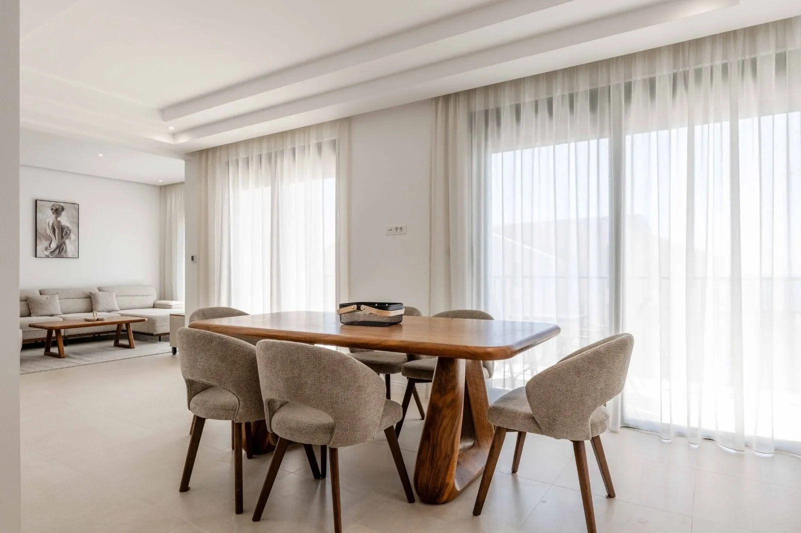 Dining area with a wooden table and upholstered chairs in a bright living room.