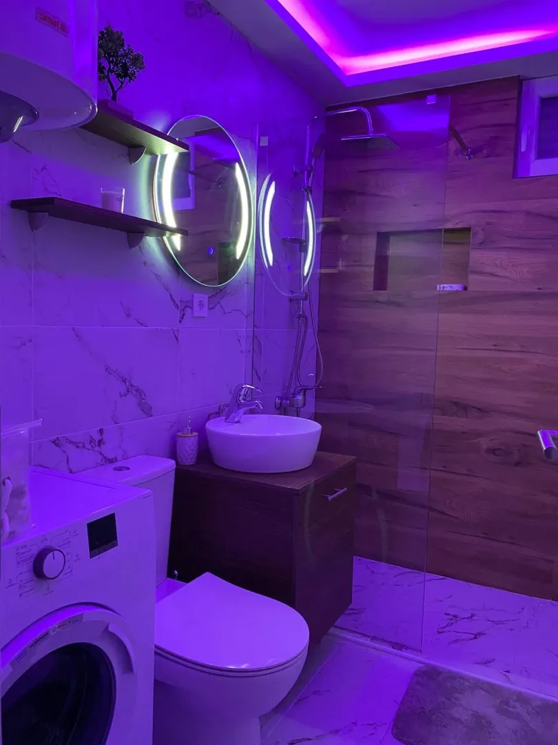 Modern bathroom with a walk-in shower, washbasin, washing machine, and decorative lighting.
