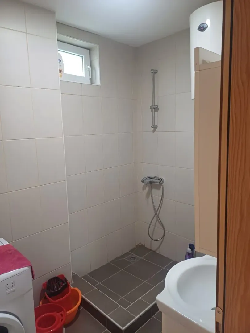 Manje kupatilo sa tuš kabinom, umivaonikom i pločicama u neutralnim tonovima.