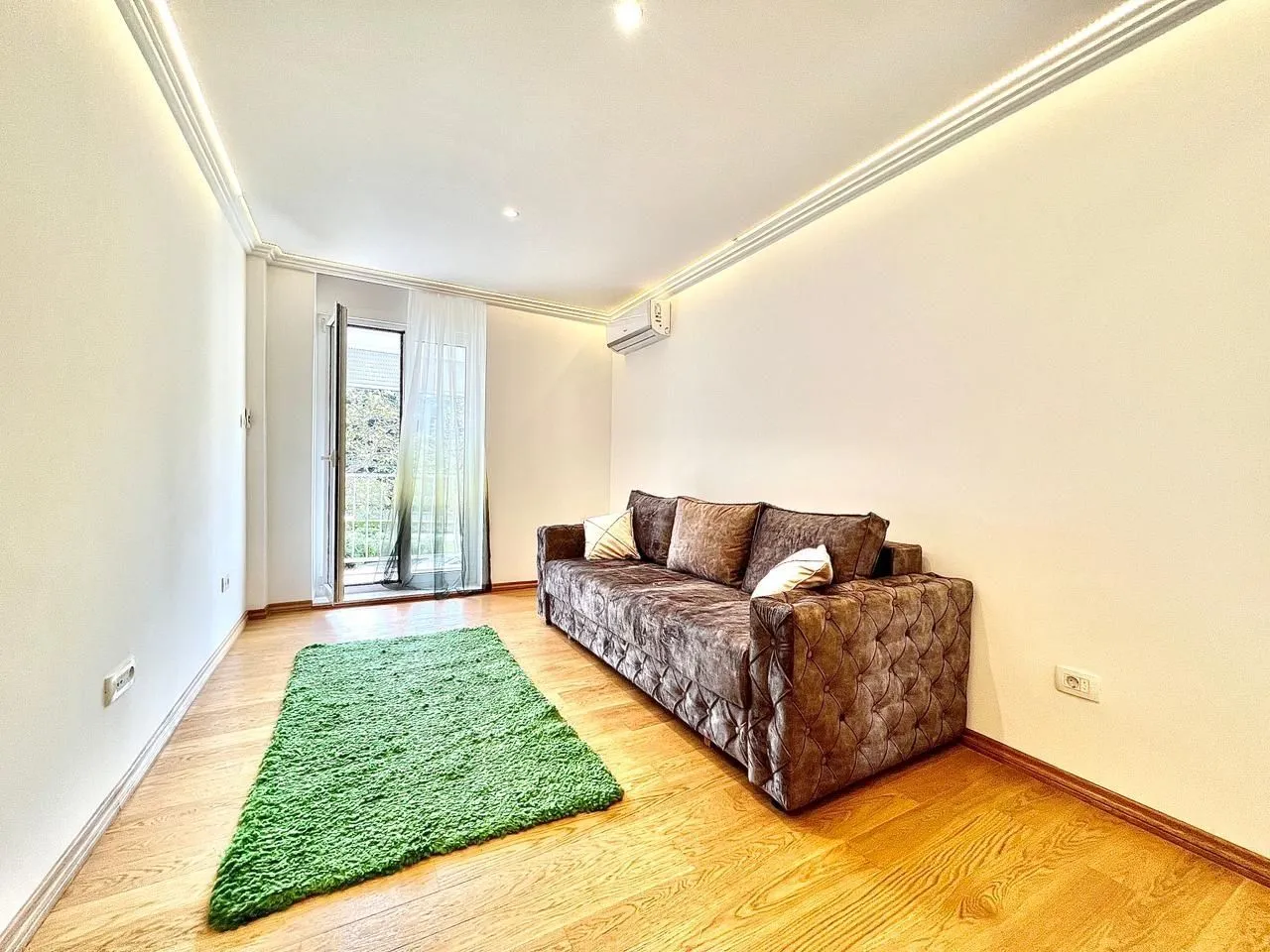 Bright living room with a comfortable sofa, a green rug, and balcony access.