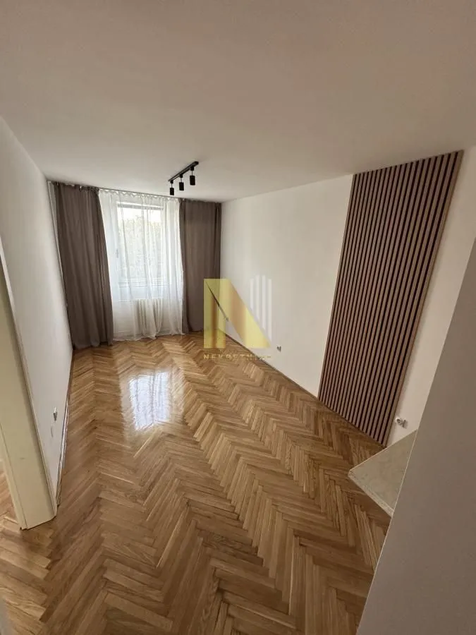 Prazna soba sa parketom i drvenim zidnim panelom.