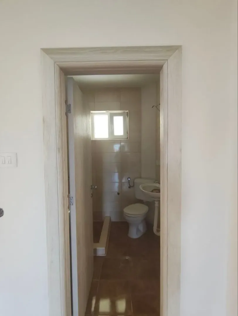 Pogled kroz vrata na kupatilo sa sanitarijama i prozorom.