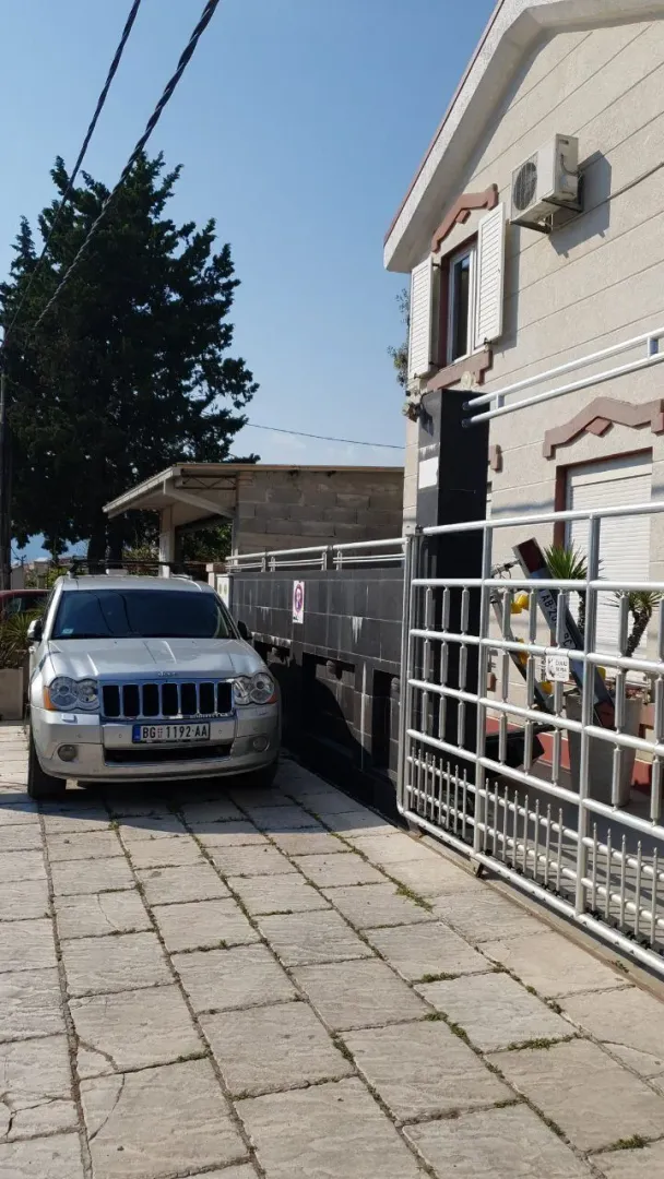 Dio dvorišta ispred kuće sa metalnom kapijom i parkiranim vozilom.