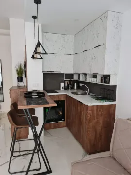 Modern kitchen with white marble-patterned cabinets, wooden work surface and a breakfast bar with stools. - image 2