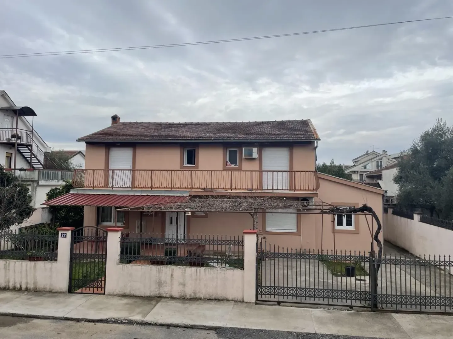 Pogled na prednju fasadu dvospratne kuće sa ogradom i dvorištem.
