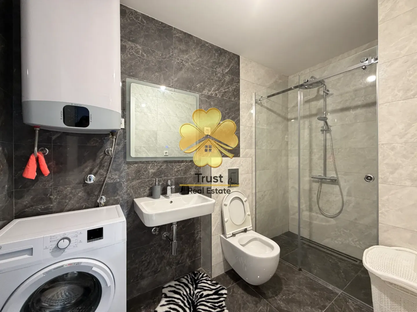 Modernly equipped bathroom with a walk-in shower, washbasin, and washing machine.
