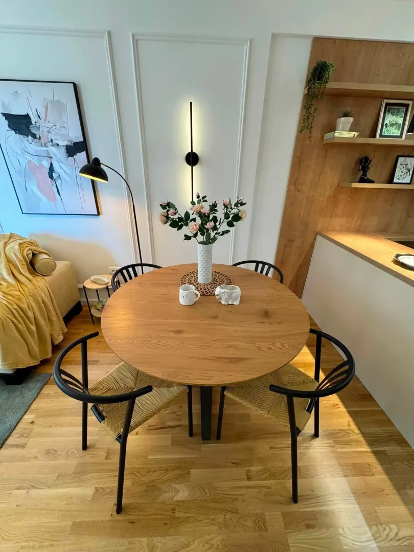 Modern dining area with a round wooden table and black chairs.