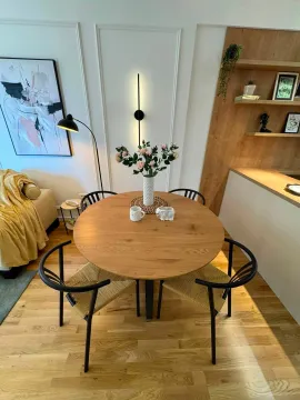 Modern dining area with a round wooden table and black chairs. - image 4