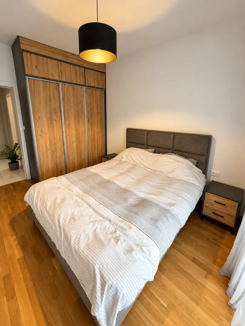 Modern bedroom with a double bed, large wooden wardrobe, and bedside tables.