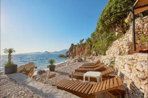 Plaža sa drvenim ležaljkama pored mora. - image 2