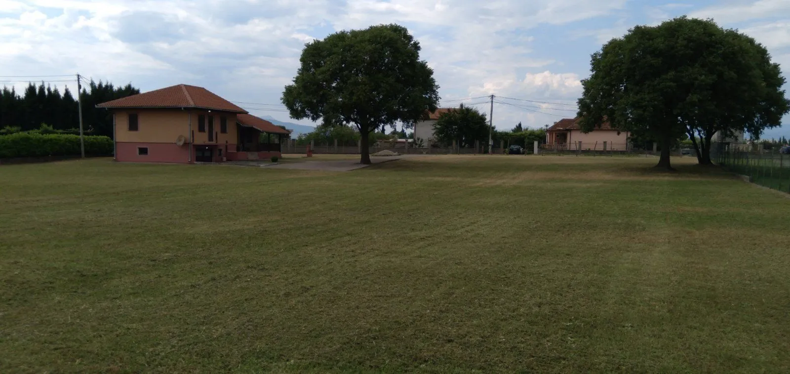 Prostrano dvorište sa travnjakom i kućom u pozadini.