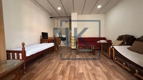 Living room with beds, sofa, coffee table, and a small kitchen area in the background. - image 4