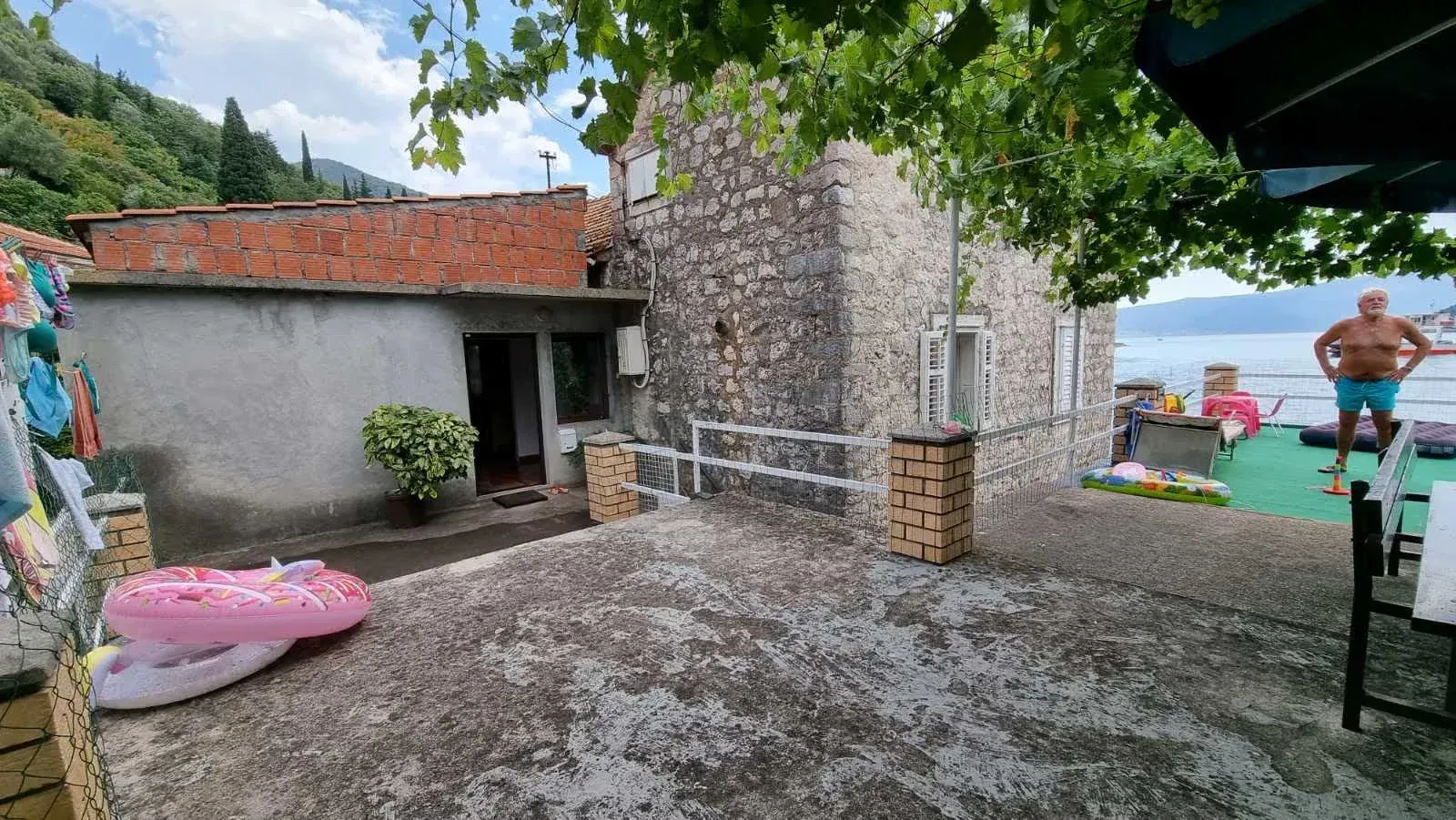 Dvorište kamene kuće sa pogledom na more i zelenilom.