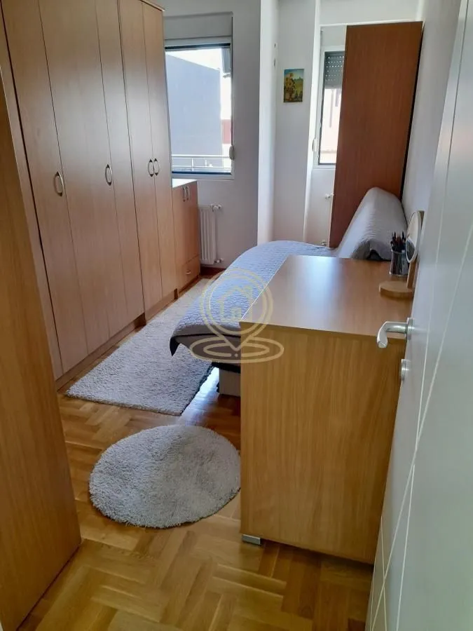 Manja spavaća soba sa krevetom, velikim plakarom i parketom na podu.