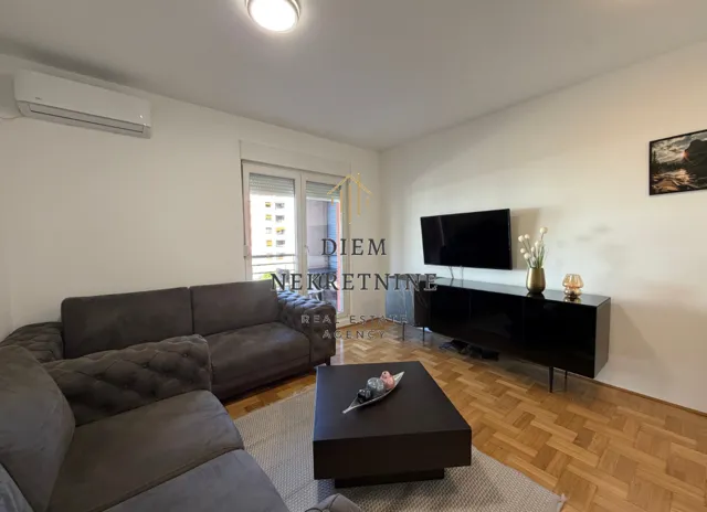 Comfortable living room with a sectional sofa, TV, and parquet flooring.