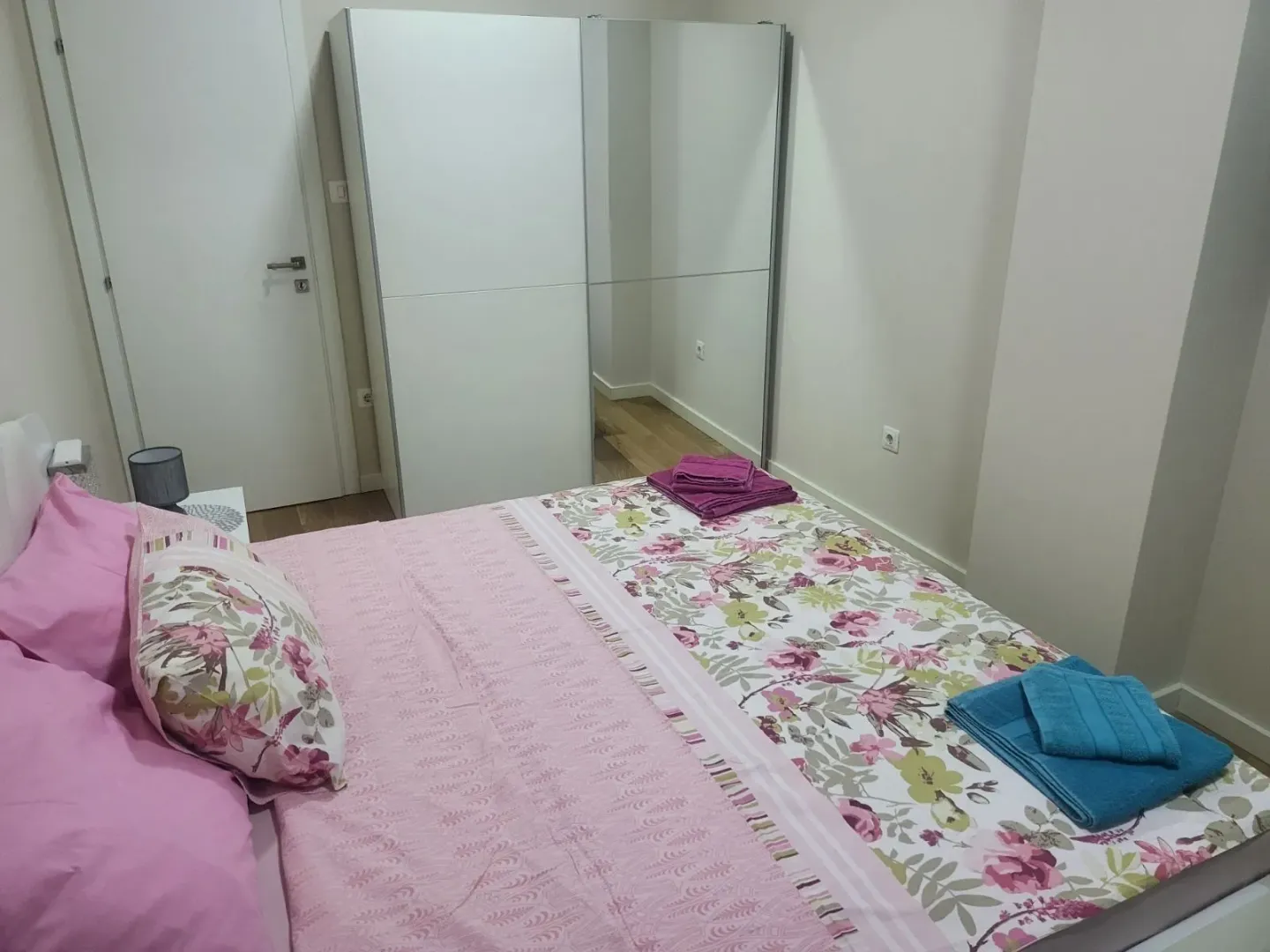 A bright bedroom with a double bed and a large white wardrobe.