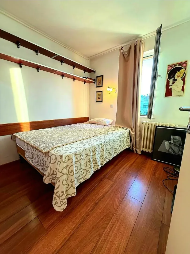 Furnished bedroom with a double bed, wooden floor and a window.