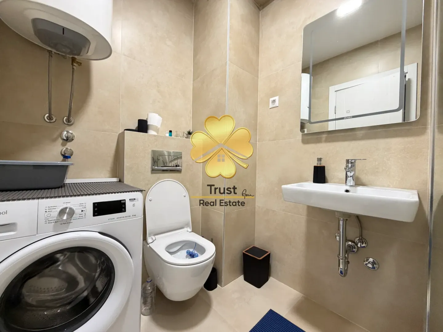 Moderno opremljeno kupatilo sa veš mašinom, umivaonikom i wc šoljom u bež tonovima.