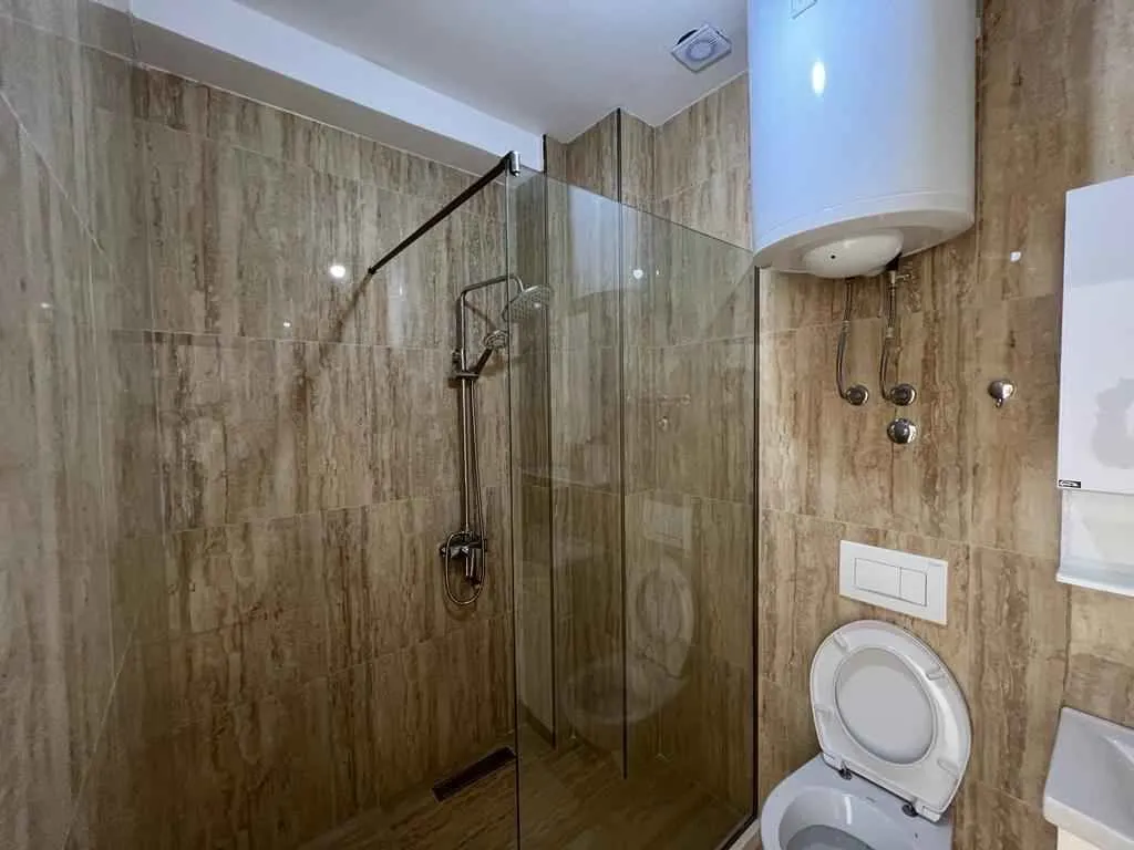 Moderno kupatilo sa staklenom tuš kabinom i pločicama u toplim tonovima.