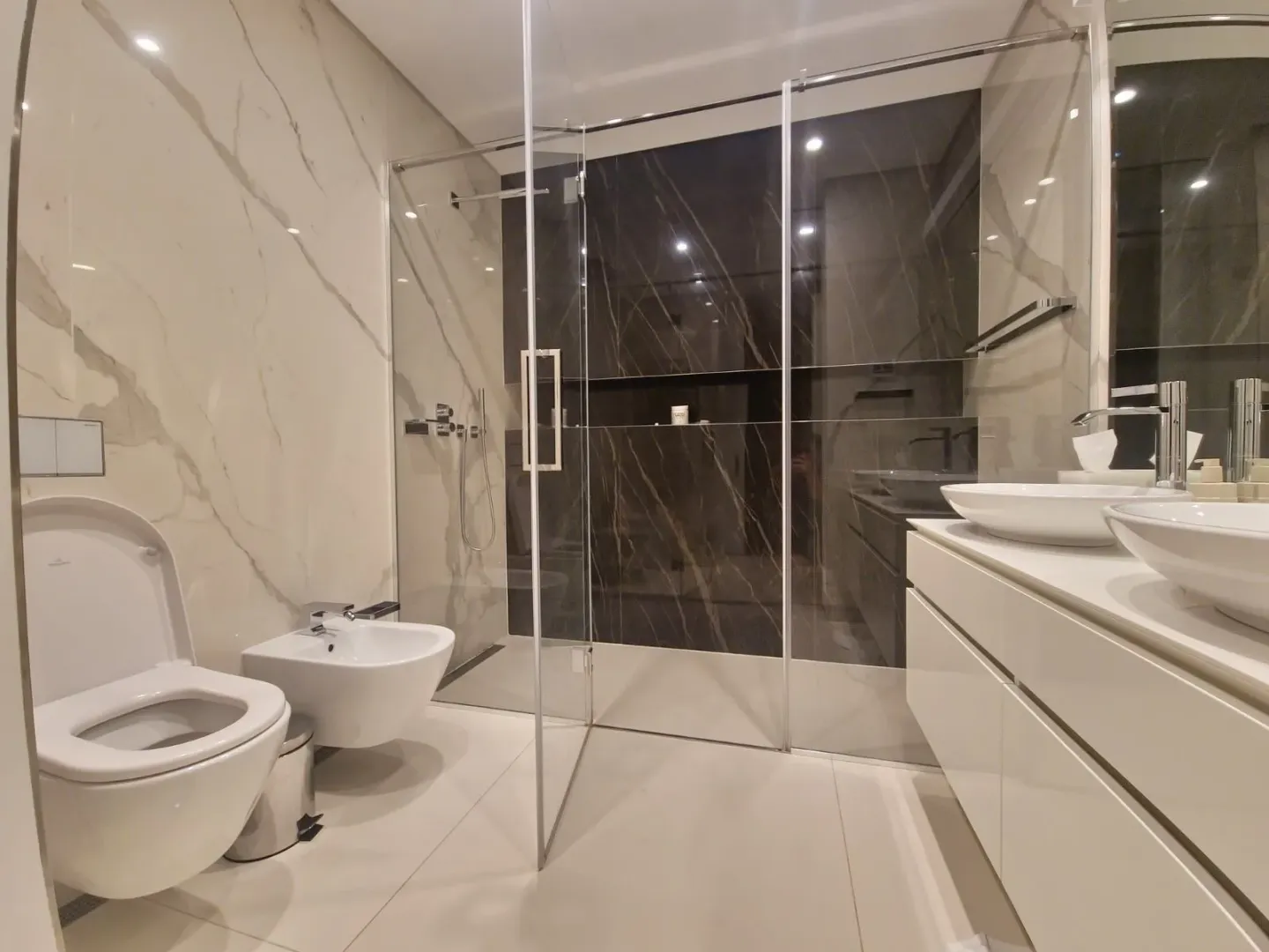 Modern bathroom with a walk-in shower, double vanity, and toilet.