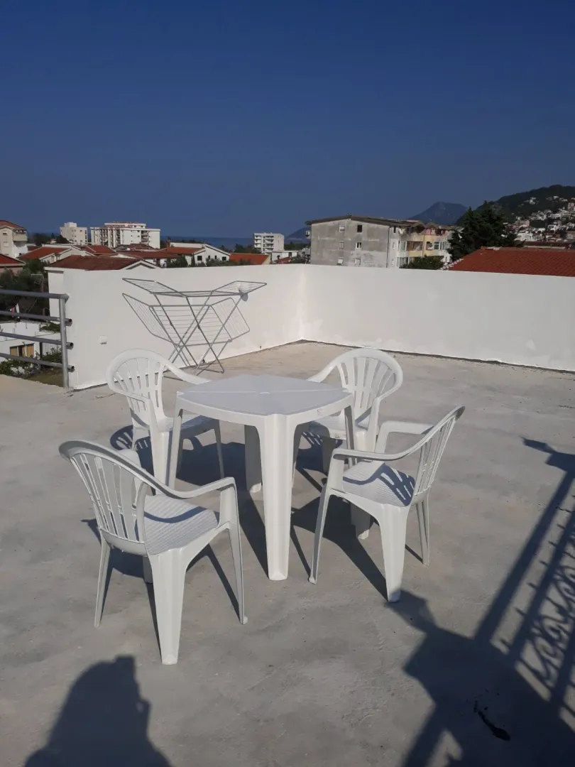 Rooftop terrace with white plastic table and chairs and surrounding view.