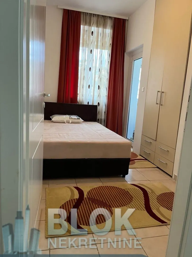 Namještena spavaća soba sa bračnim krevetom, plakarom i izlazom na terasu.