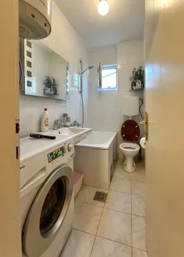 Smaller bathroom with a bathtub, washbasin, washing machine, and toilet. - image 8