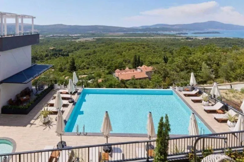 Pogled sa terase na bazen i okolni pejzaž sa morem u daljini.