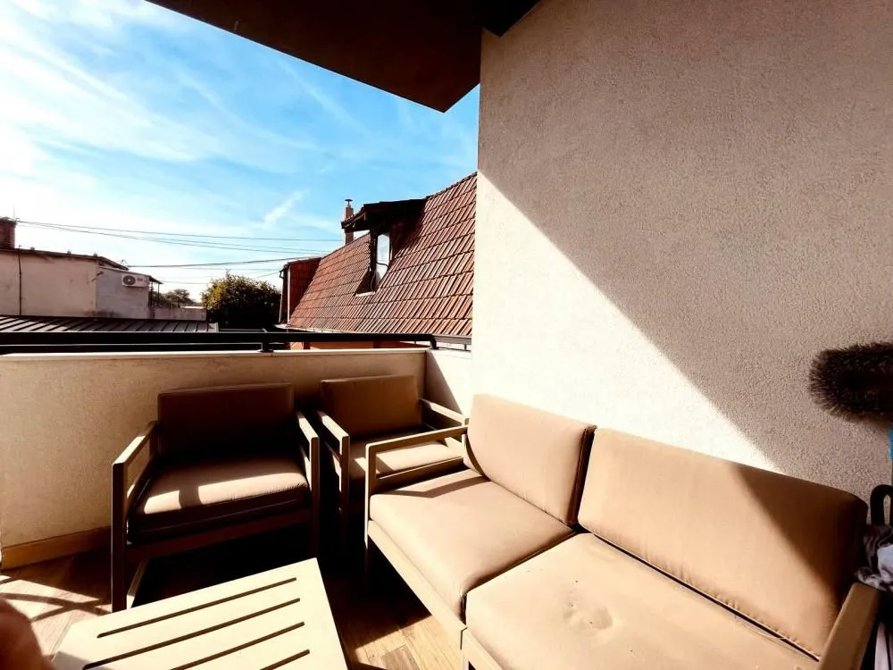 Namešten balkon sa garniturom za sedenje i pogledom na okolne krovove.