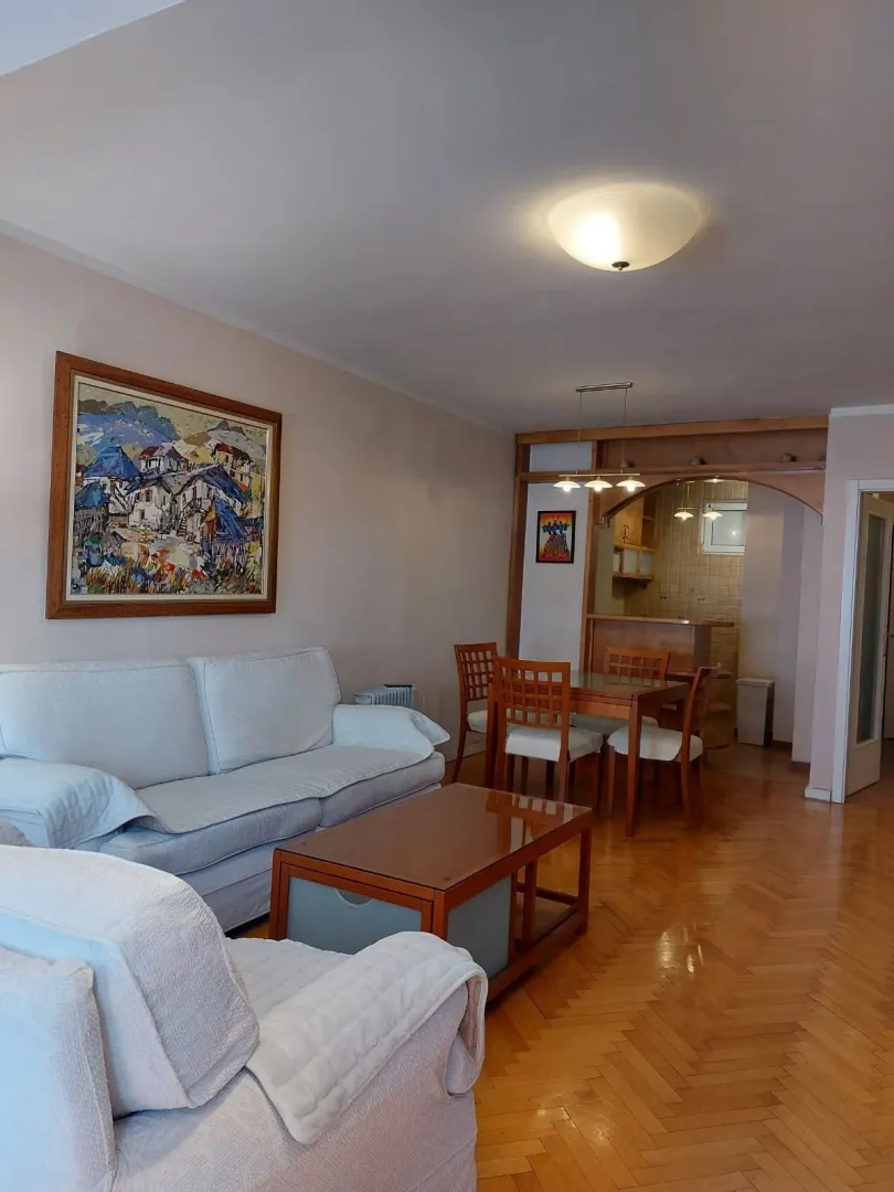 Svijetla dnevna soba sa garniturom za sjedenje i trpezarijom u pozadini.