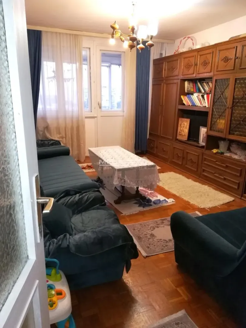 Dnevna soba sa garniturom, velikim drvenim ormarom i izlazom na terasu.