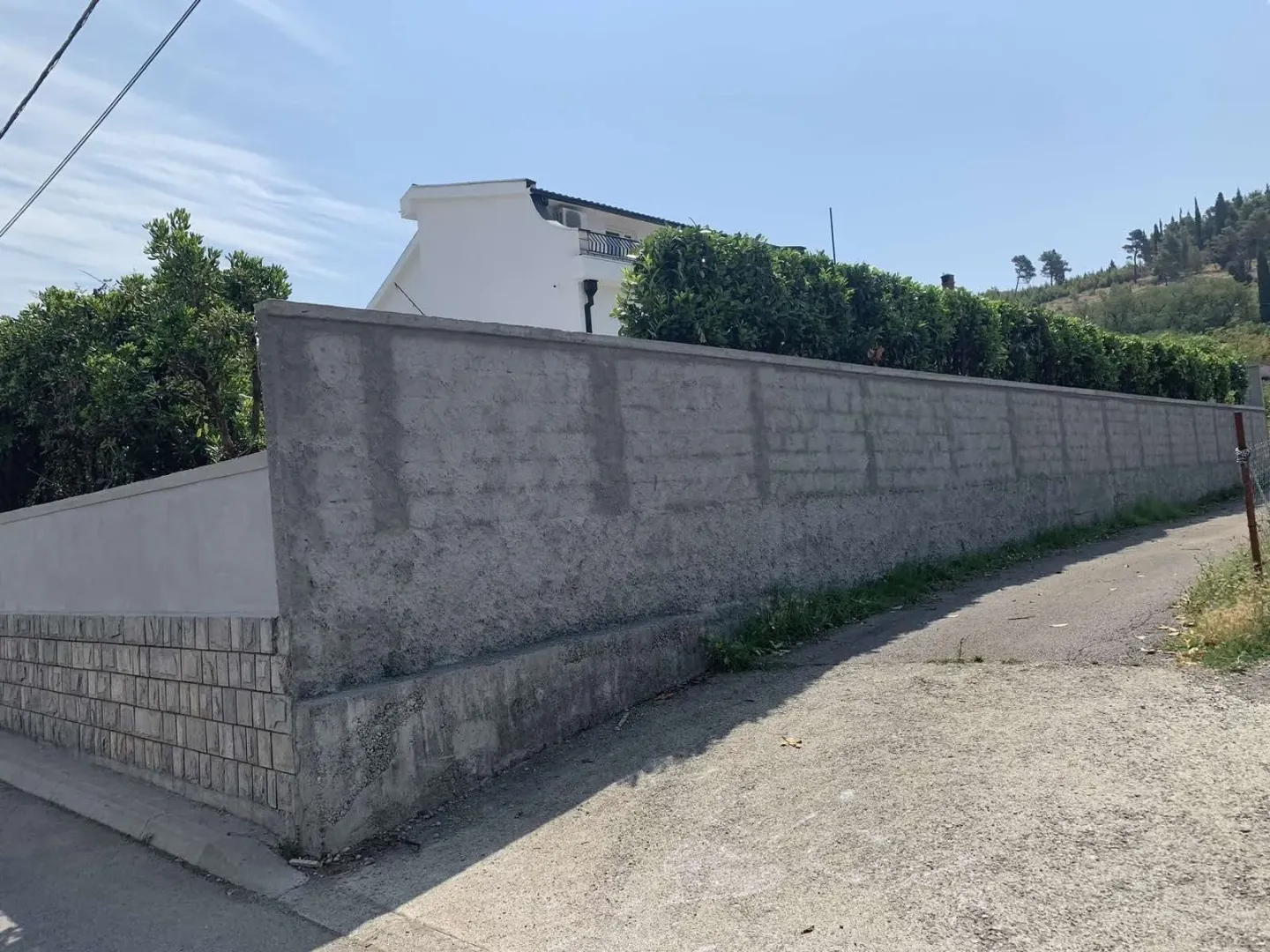 Concrete wall around a house yard with a green hedge.