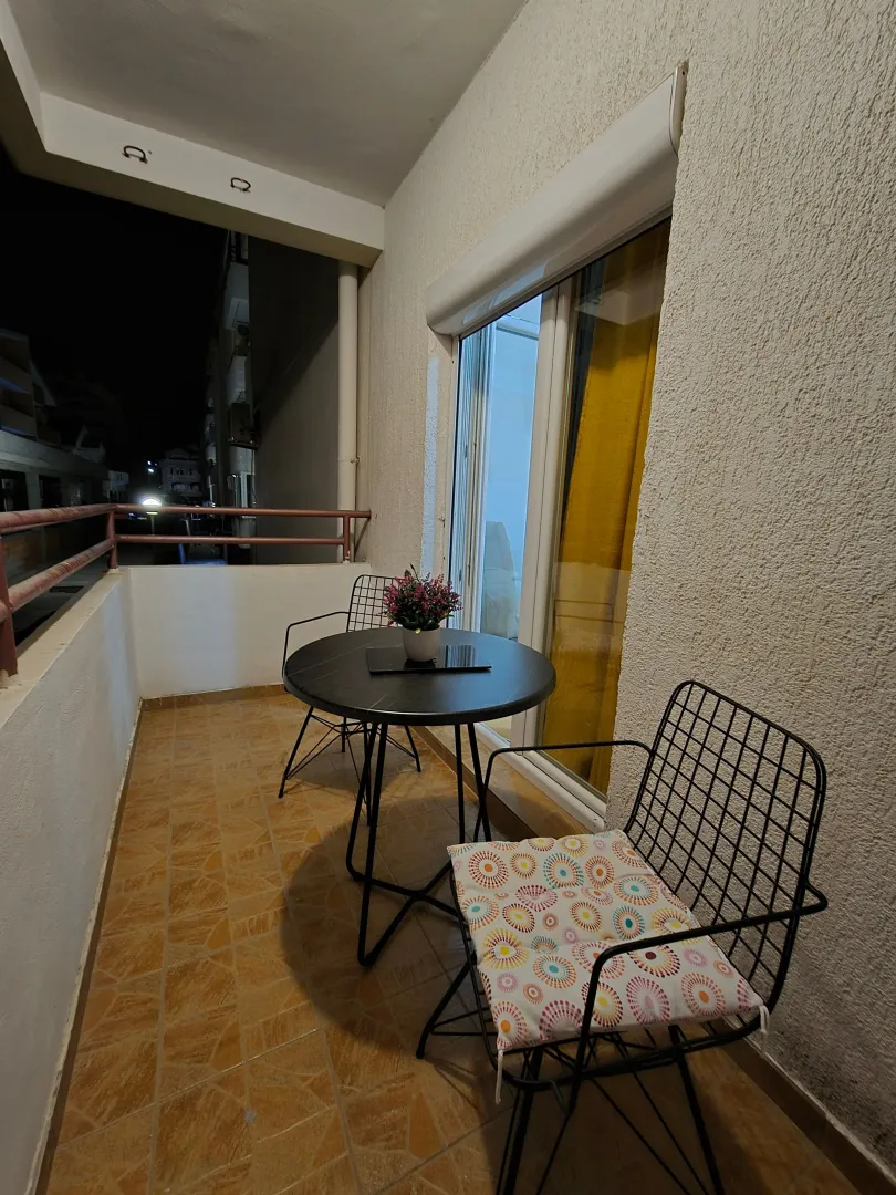 Furnished balcony with a table and two chairs in a night setting.